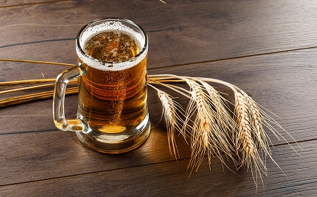 Стеклянная кружка пива с пеной и колосья пшеницы на деревянном столе